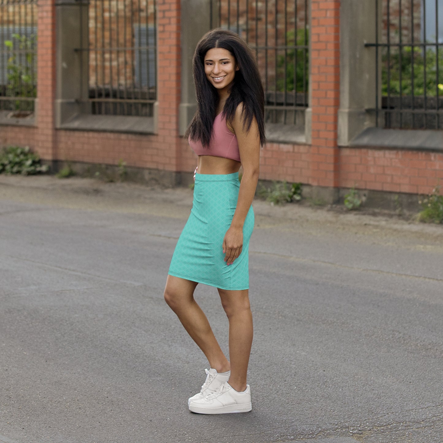 Woman in a pink crop top and turquoise skirt standing on a street with a brick building in the background.