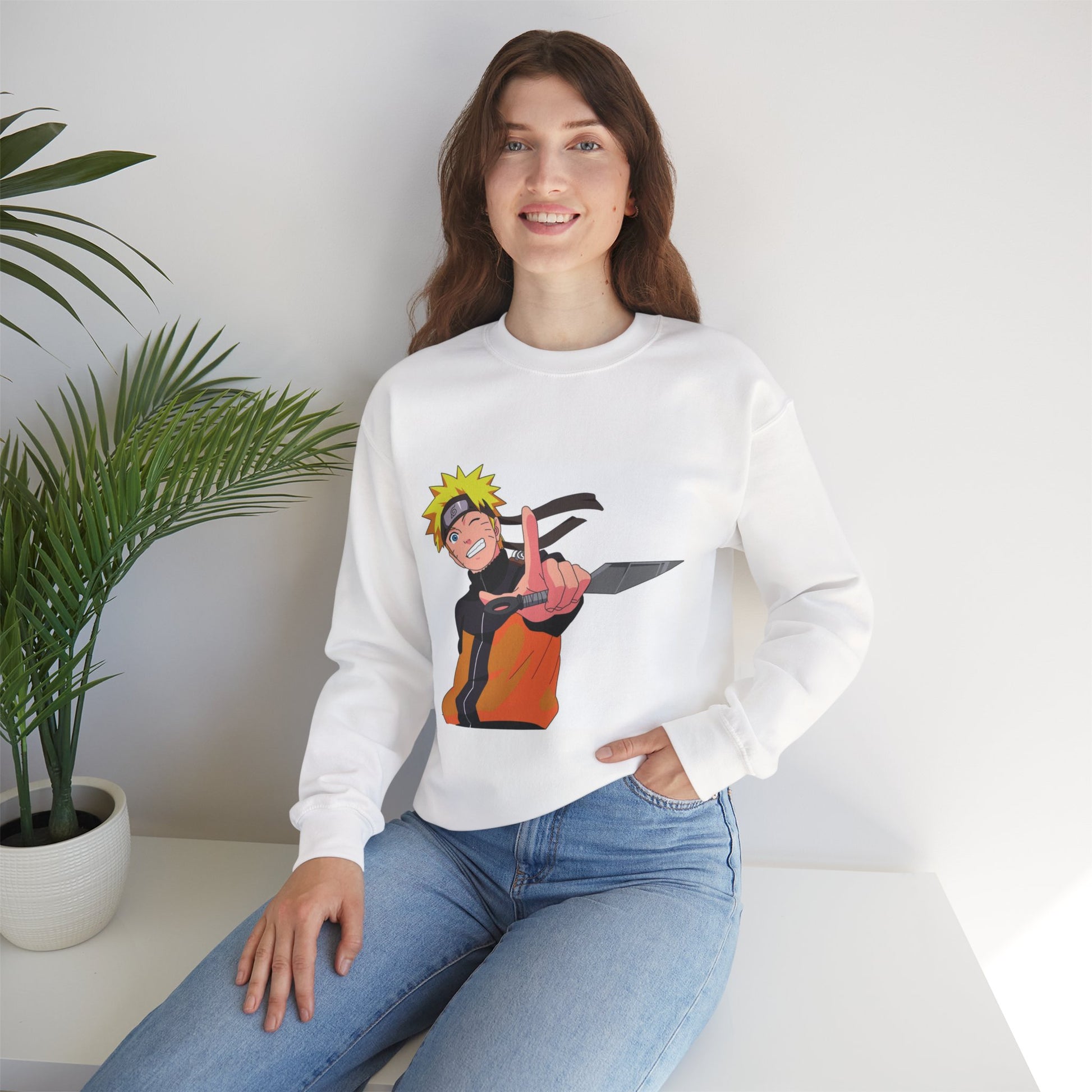 Person wearing a white sweatshirt with a graphic design, sitting in a room with a plant.