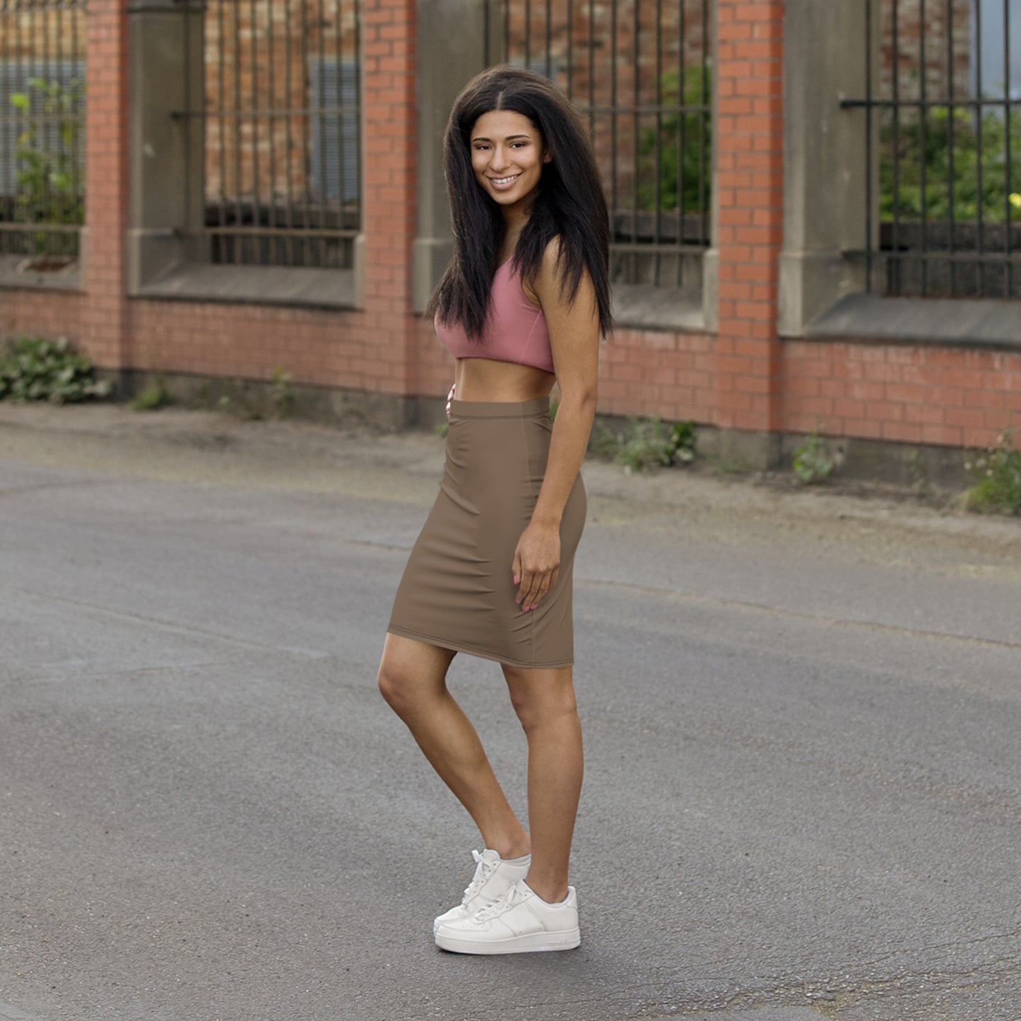 Woman in pink crop top and brown skirt standing on a street with a brick building in the background