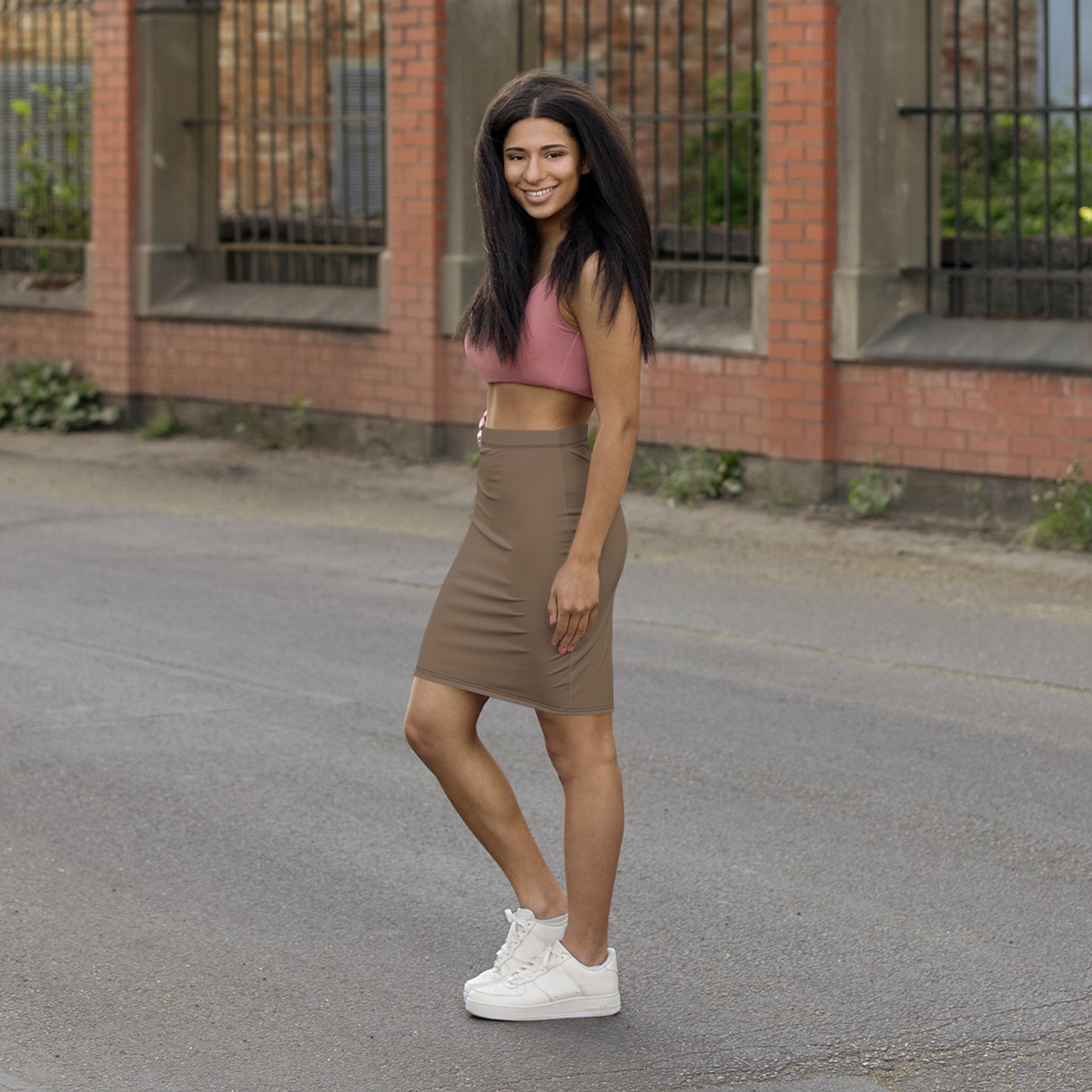 Woman in pink crop top and brown skirt standing on a street with a brick building in the background