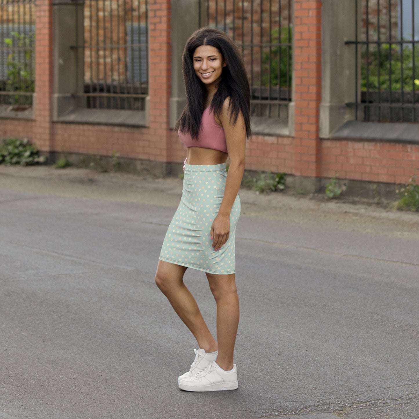 Woman in a green skirt and pink top standing on a street with a brick building in the background