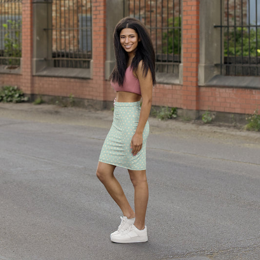 Woman in a green skirt and pink top standing on a street with a brick building in the background